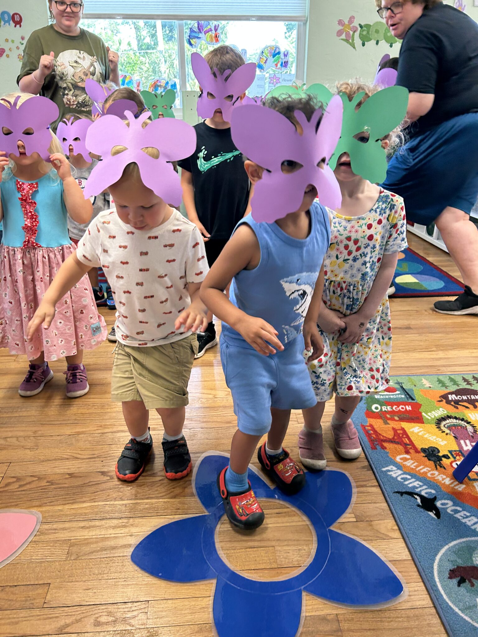 A group of two and three year olds with butterfly masks on dancing on a flower cut out