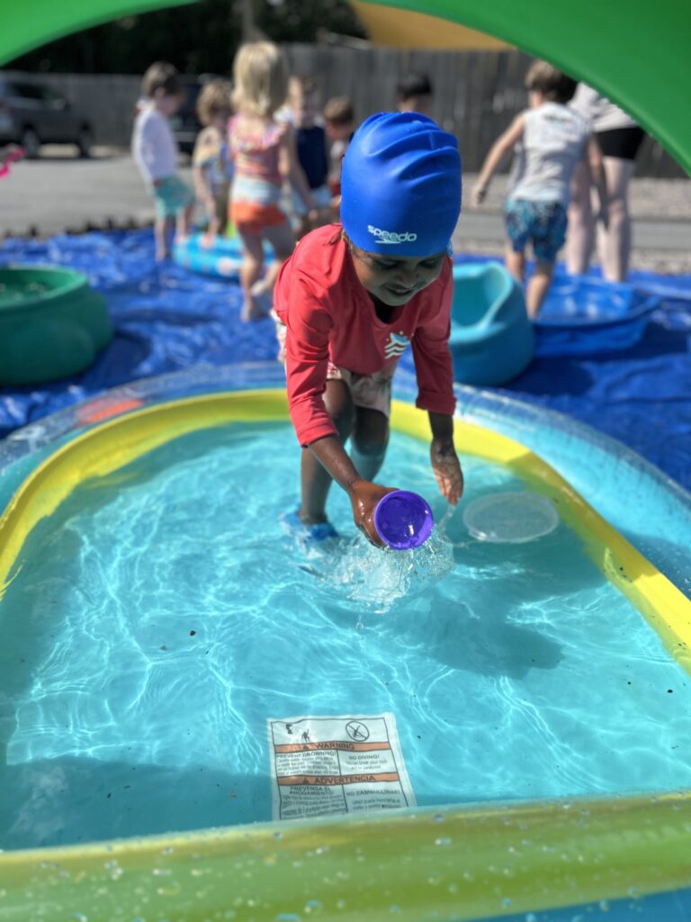 IMG_4928 A two year old girl with a swim cap on in a splash pool outside for water day