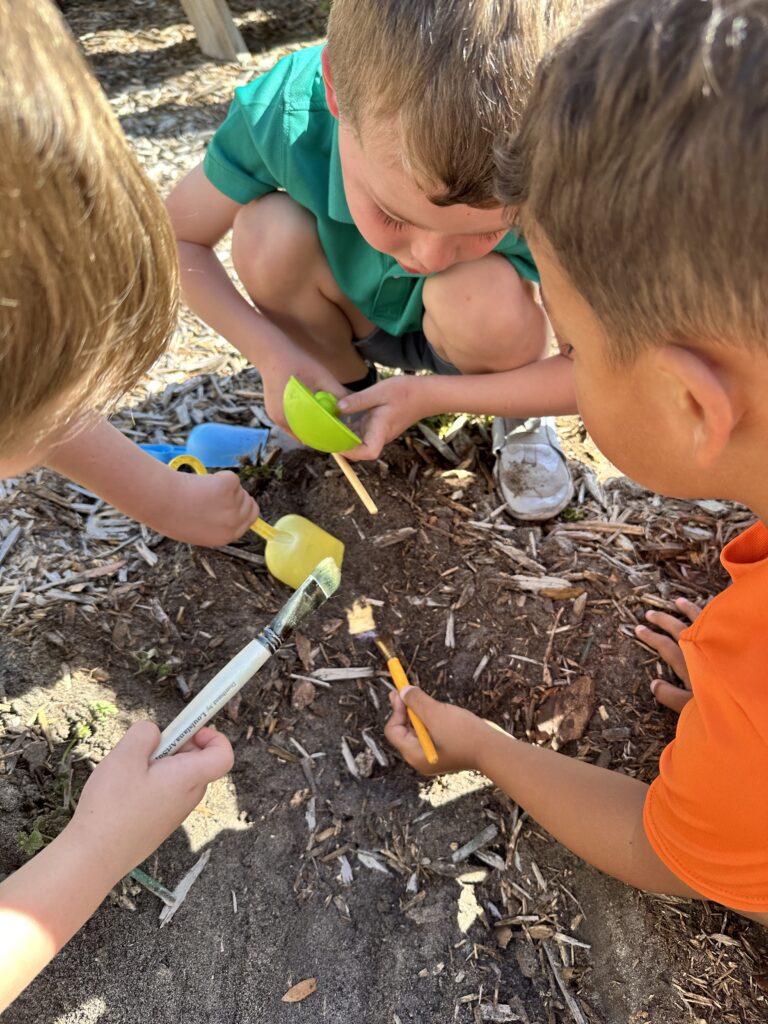 IMG_9203 3 four year old boys digging up dinosaur bones outside with shovels and paintbrushes